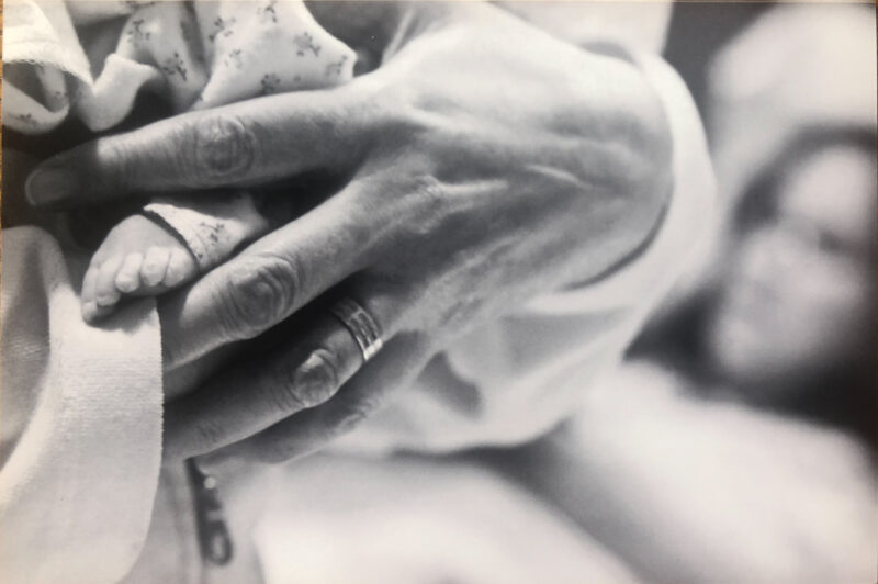 premie baby foot, black and white being held by fathers hand